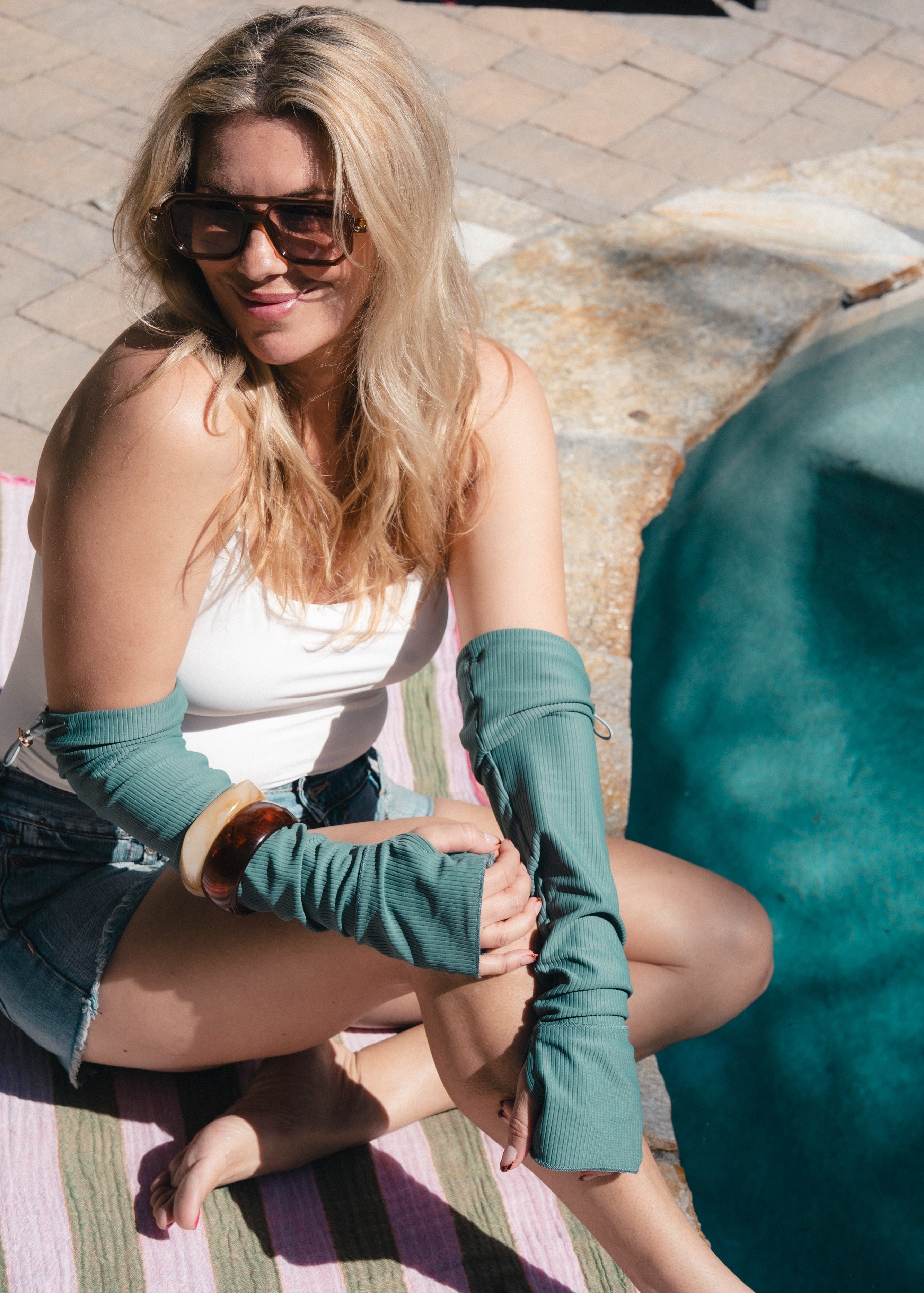 Woman sitting outdoors wearing teal arm sleeves and sunglasses.