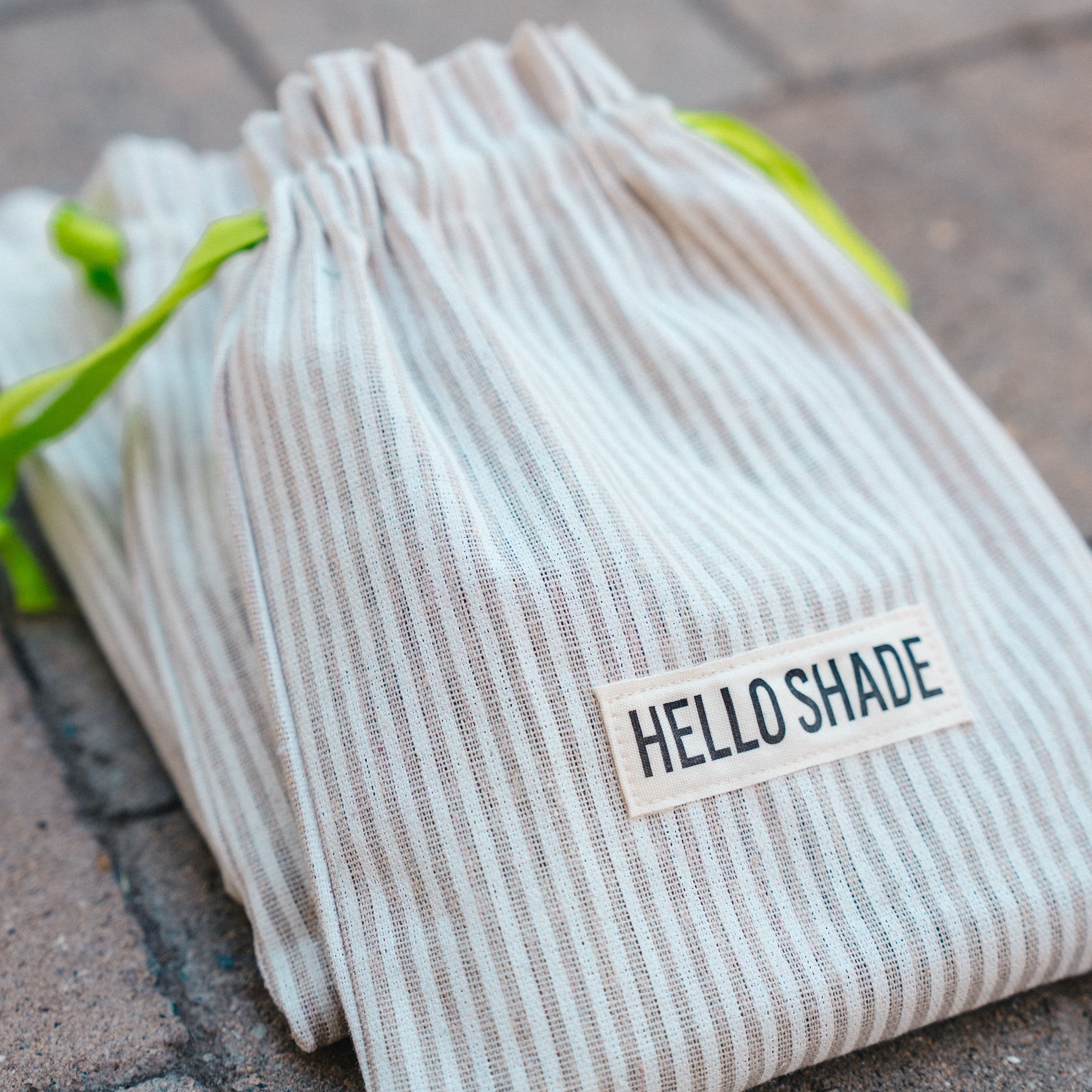 Striped fabric bag with 'HELLO SHADE' label on a textured surface
