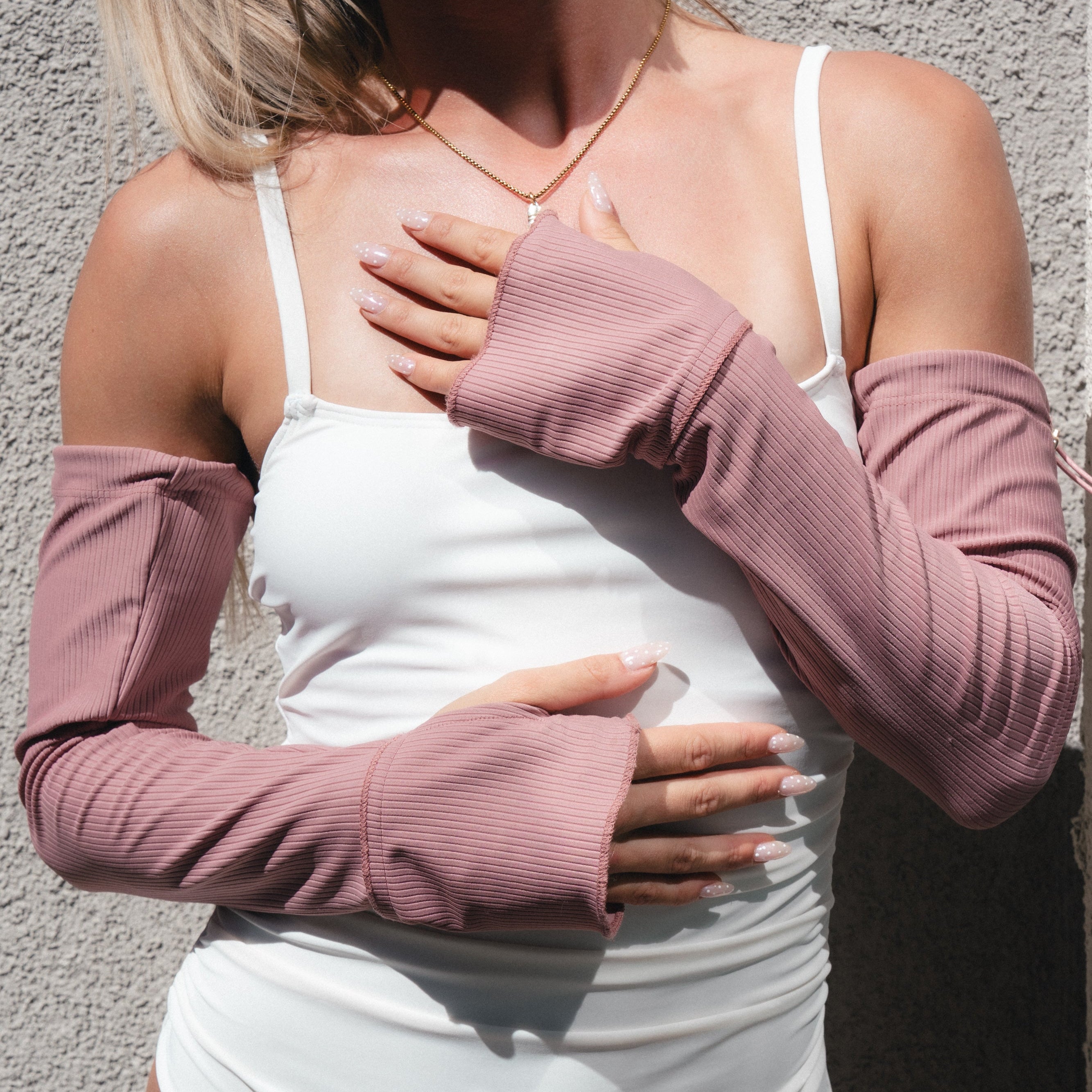 Woman wearing a white top and pink arm sleeves against a gray wall.