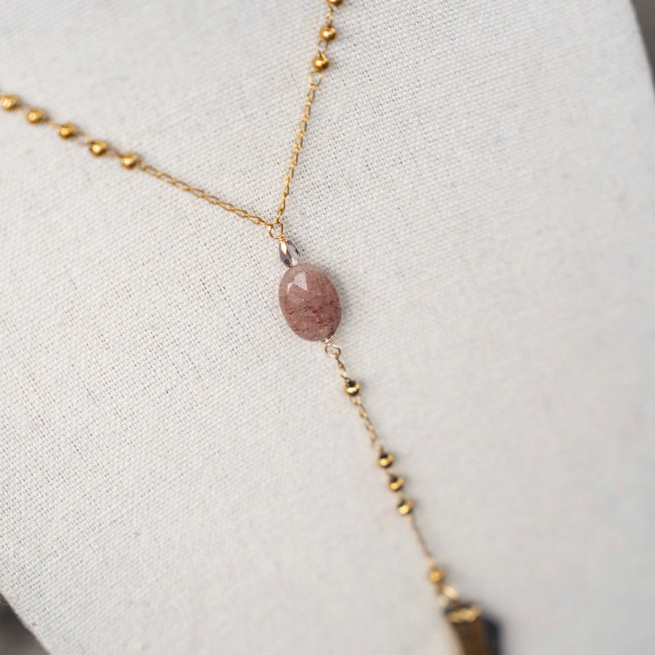 Necklace with a pink stone and gold chain on a white surface
