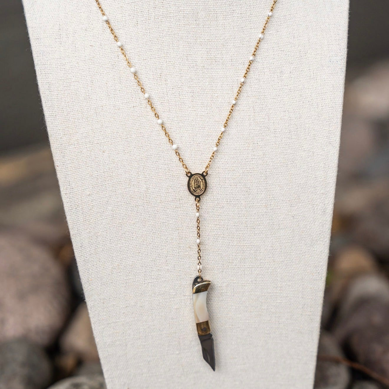 Necklace with a pendant on a white stand against a natural stone background