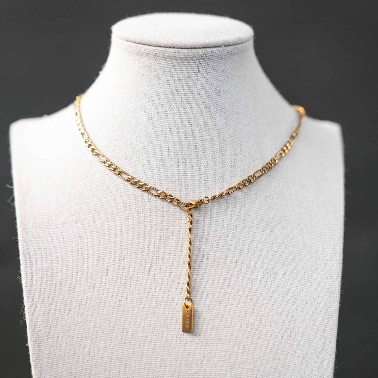 Gold chain necklace with a pendant on a mannequin bust against a dark background