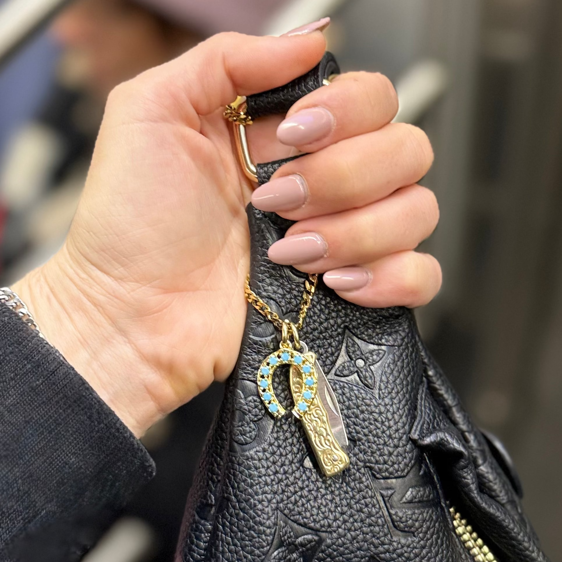 Hand holding a black patterned handbag with a keychain on a blurred background