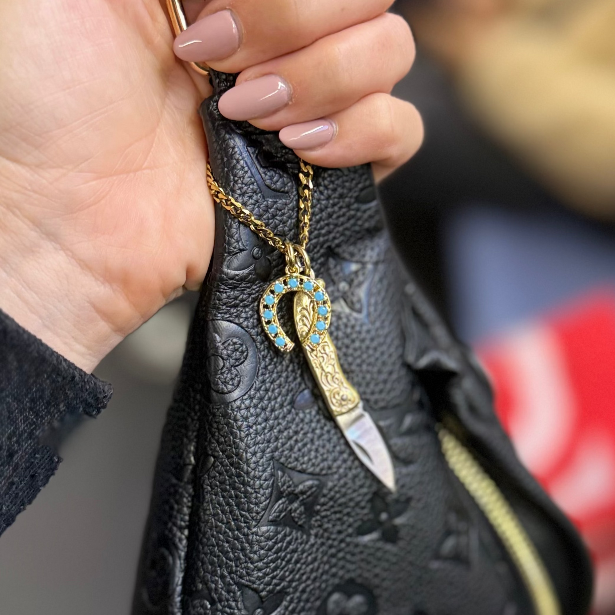 Hand holding a black textured handbag with a decorative clasp, blurred background